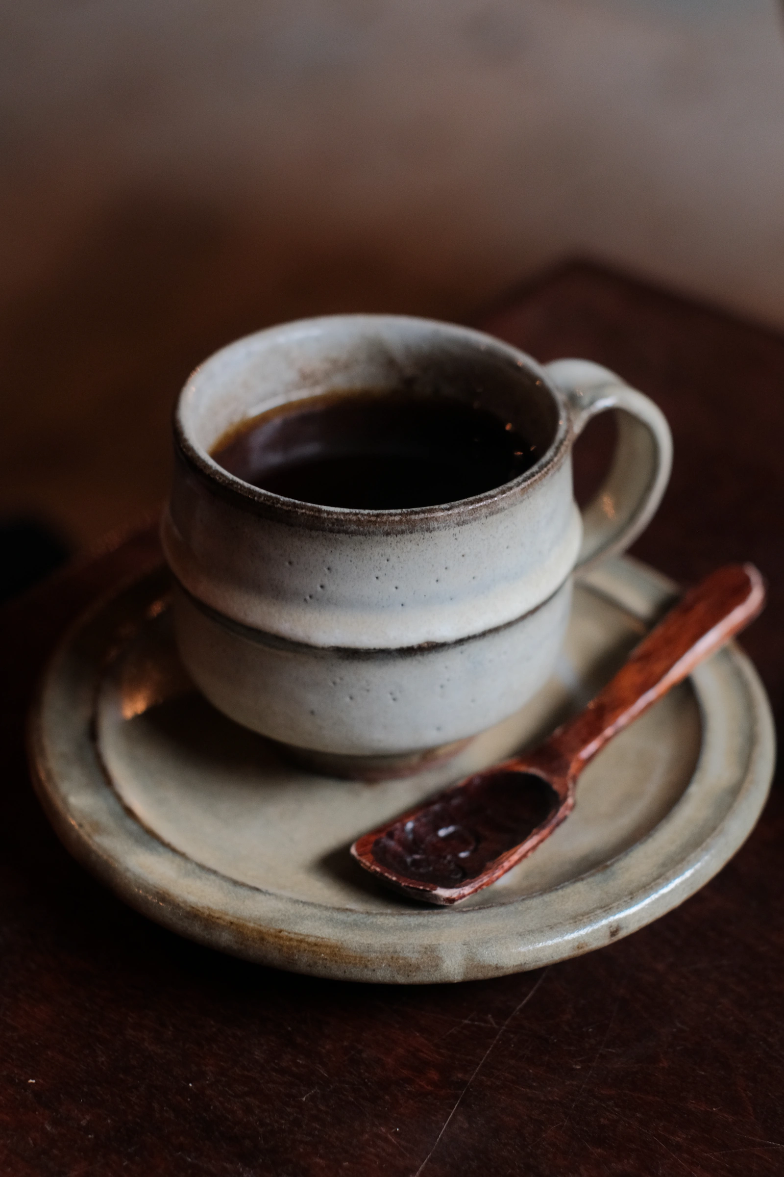 A cup of black coffee on a ceramic saucer with a small wooden spoon