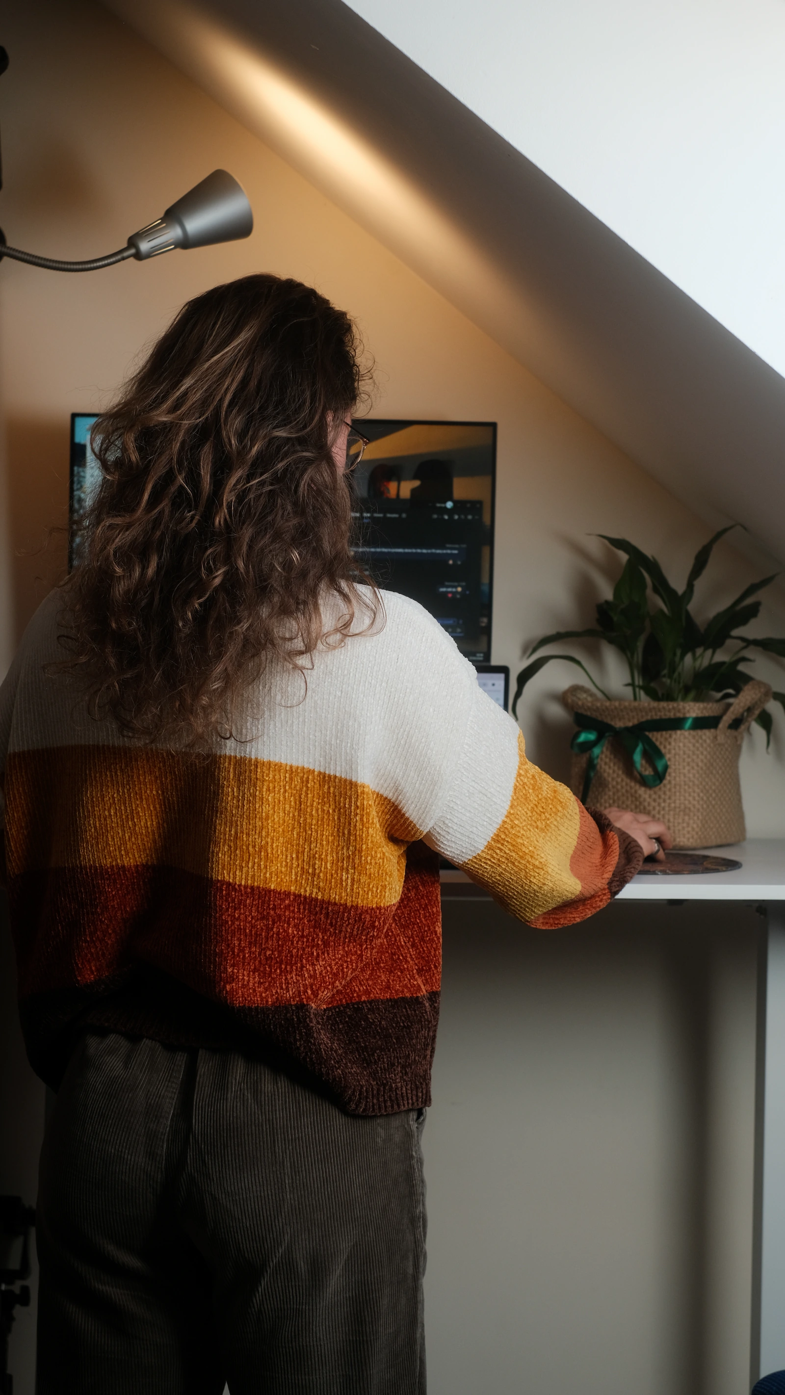 Vika working at a standing desk, viewed from behind, with a monitor and a plant nearby