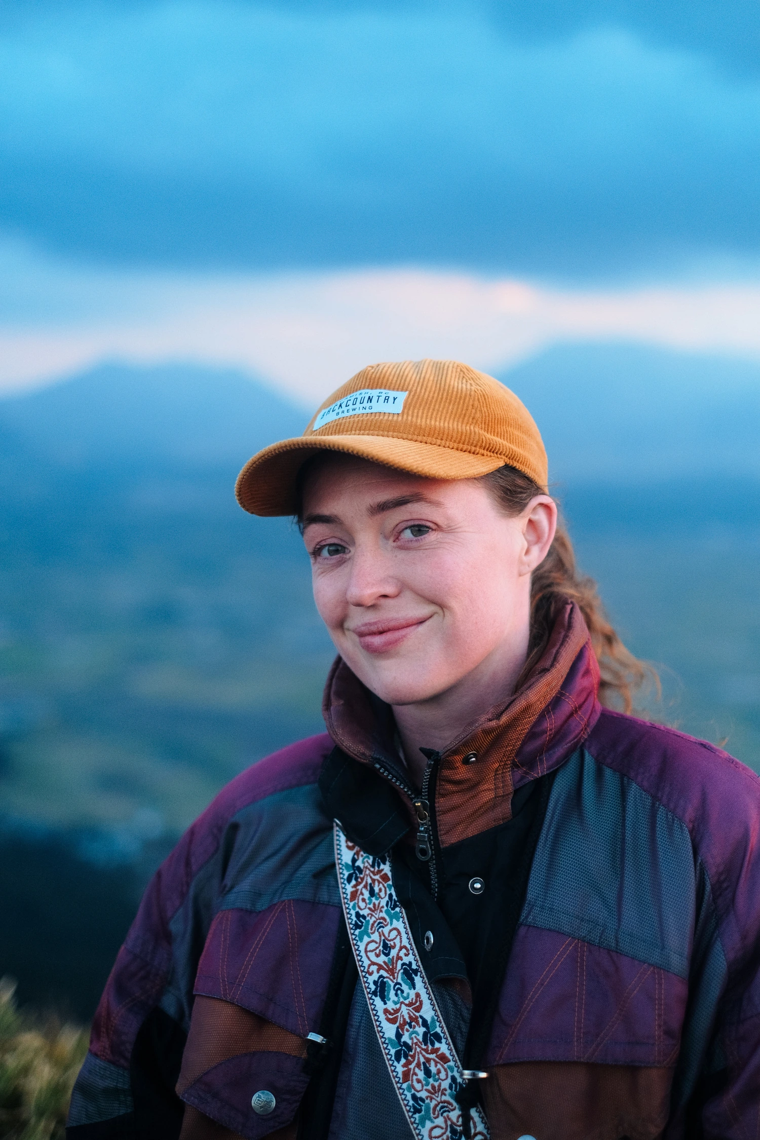 Portrait of Vika Sokolova smiling outdoors, wearing an orange cap